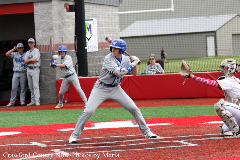 Baseball batter in gray uniform and blue helmet swings at home plate as the catcher in white gear reaches to tag on the right.