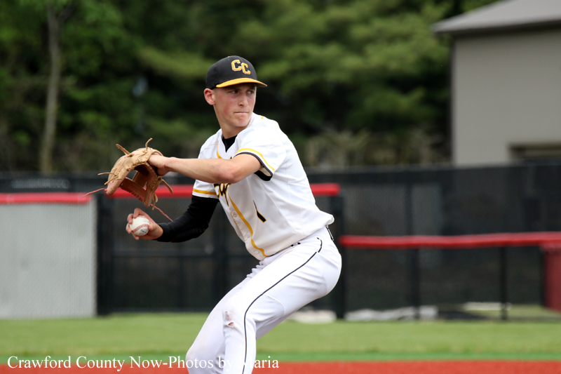 Baseball pitcher in white and black-yellow uniform throwing a pitch on a grassy field, glove cocked and ready to release the ball.