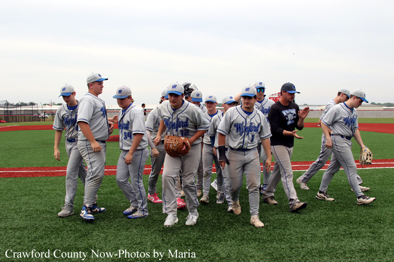 Youth baseball team in gray uniforms walks together on a baseball field, gloves on and caps on their heads.