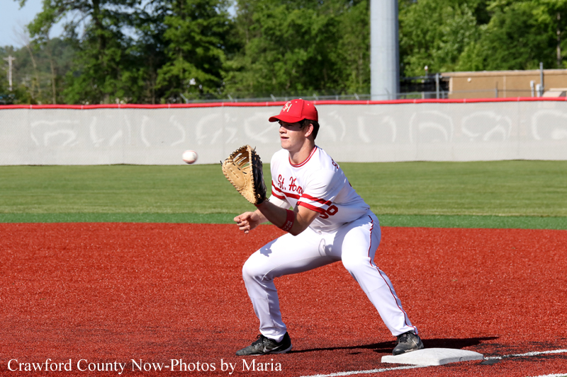 Baseball pitcher in a white and red uniform crouches on the pitcher's mound, glove up, ready to throw as a ball approaches from the left.