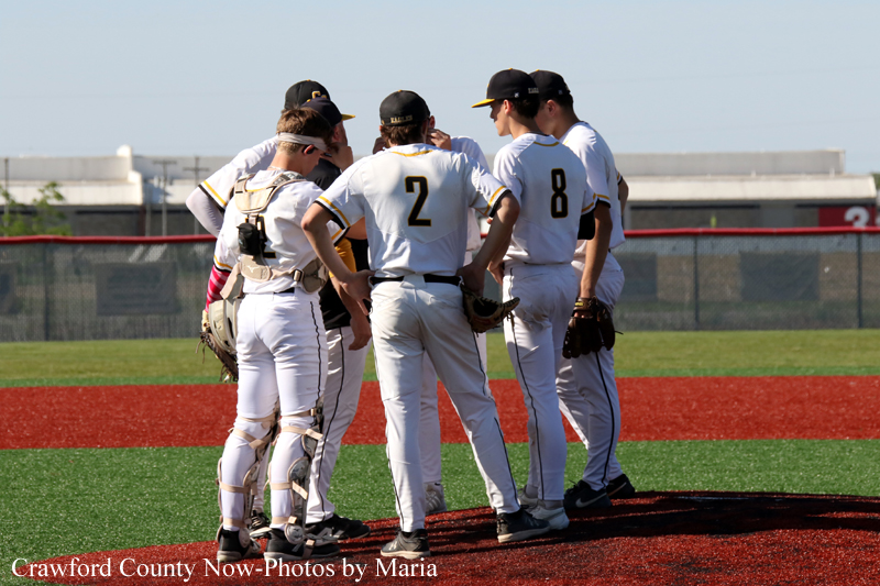 Baseball players in white uniforms huddle on the infield before a game on a sunny day.