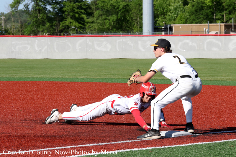 Baseball tag play: runner in red helmet slides toward the base while a fielder in white crouches to tag him at the bag.