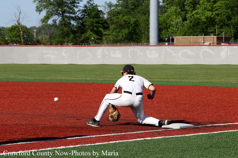 Baseball infielder in white uniform with number 2 stretching to field a ground ball on the red infield dirt.