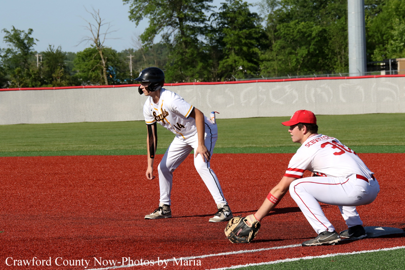 Baseball game scene: runner in white uniform stands on the red infield dirt as a fielder crouches with a glove nearby, ready to field.