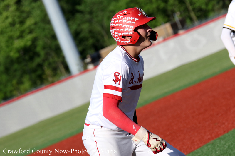 Baseball player in a white uniform with red sleeves and a red helmet, standing on the red-dirt infield of a baseball field during a game.