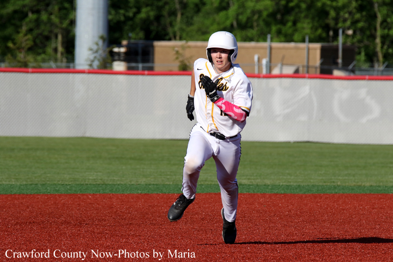 Baseball player in a white uniform running on the red infield during a game, wearing a helmet and black glove on her left hand.