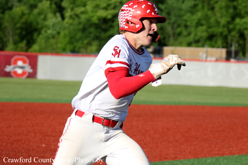 Baseball player in a white and red uniform runs on a dirt infield, wearing a red helmet and glove in mid-play.