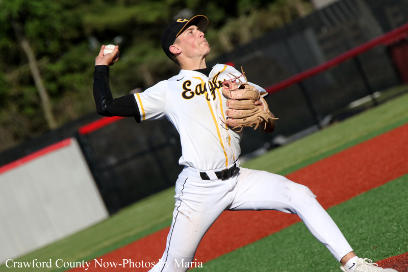 Baseball pitcher in a white uniform mid-throw on a mound, glove up, eyes on the target.