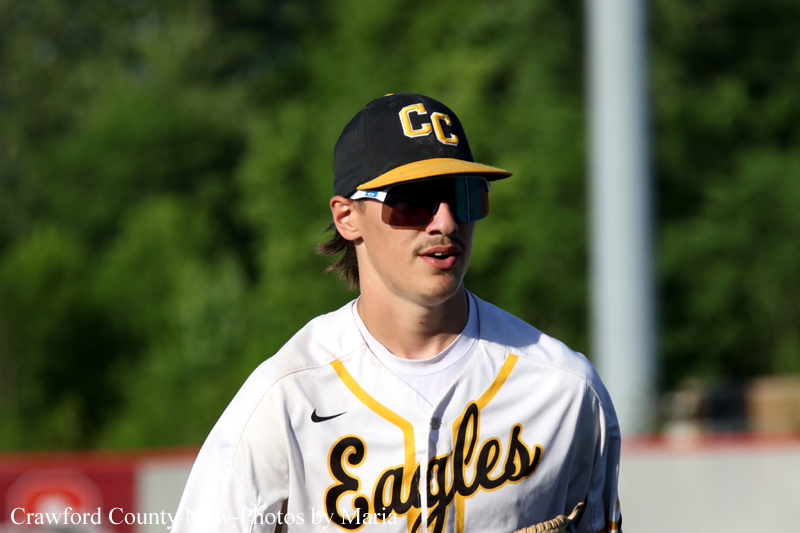 Baseball player in a white and gold Eagles jersey with a black and yellow cap, wearing dark sunglasses on the field.