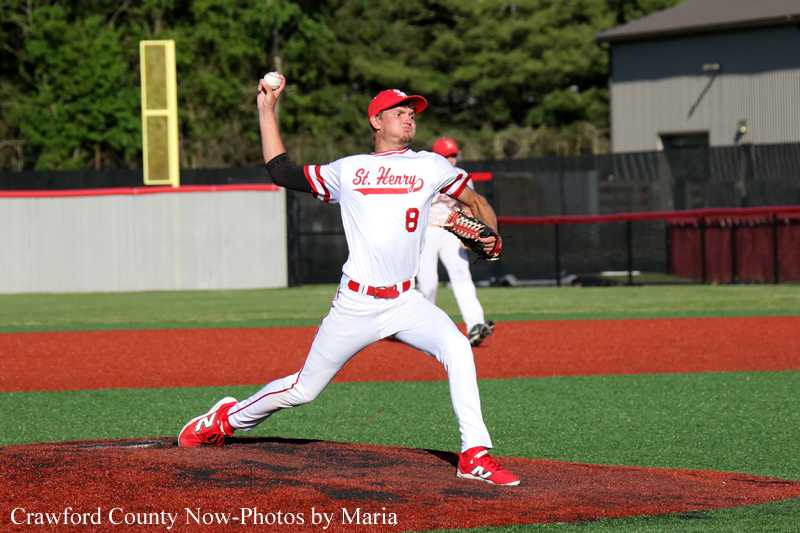 Baseball pitcher in a white-and-red uniform labeled St. Henry, mid-throw on the mound with throwing arm raised, glove on the other hand, on a green field with a red infield.