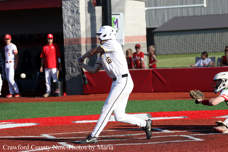 Baseball batter in a white uniform with helmet mid-swing in the batter's box, with a catcher reaching to the right and a red dugout in the background.