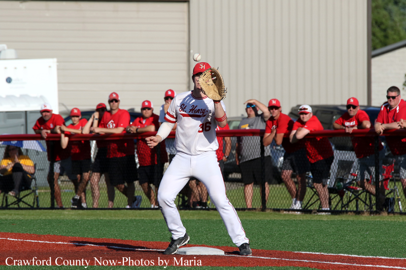 Baseball pitcher in a white uniform (number 36) winds up to throw on a red-dirt mound, with a crowd in red shirts watching from behind a fence.