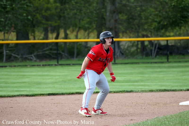 Baseball player in a red uniform crouching on the infield dirt, helmet on, ready to field the ball.