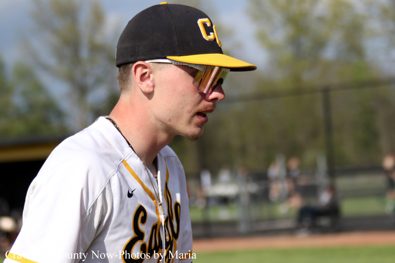 Baseball player in profile wearing a black and yellow cap and sunglasses, on a sunny field.