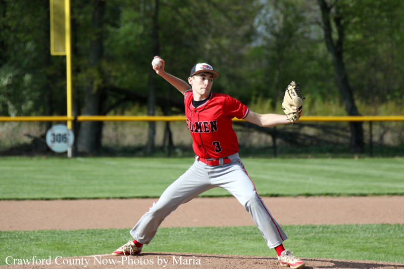 Baseball pitcher in a red uniform winds up to throw from the mound on a sunny field.