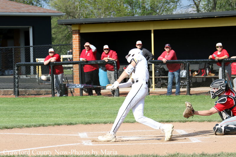 Baseball batter in white uniform swings at a pitch near home plate as the catcher in red crouches behind him.