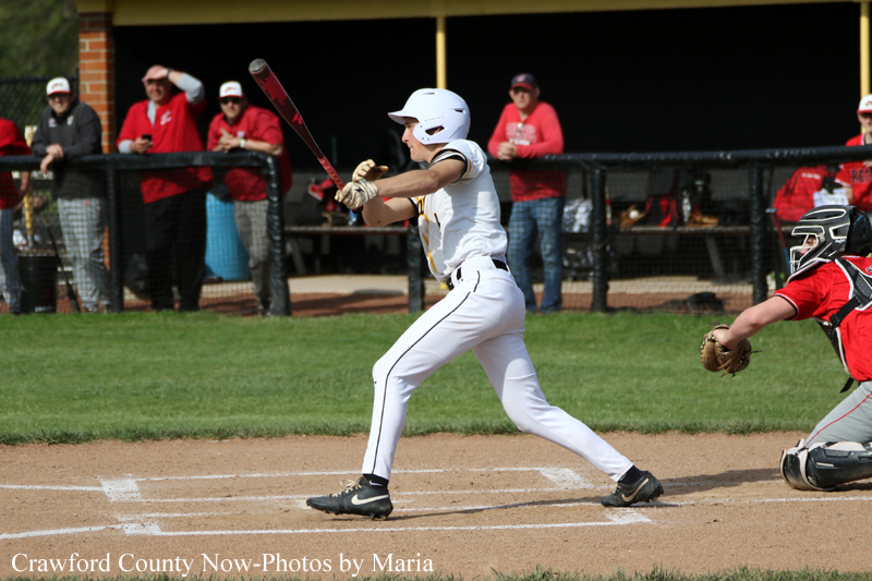 Baseball batter in white uniform swings at a pitch as a catcher in red crouches behind him on the dirt infield.