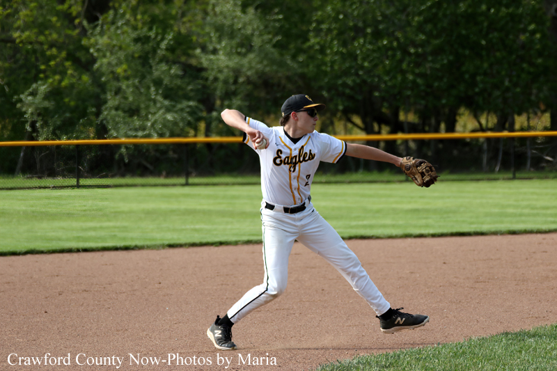 Baseball pitcher in a white Eagles uniform delivering a pitch on a dirt infield with a grassy outfield behind her.