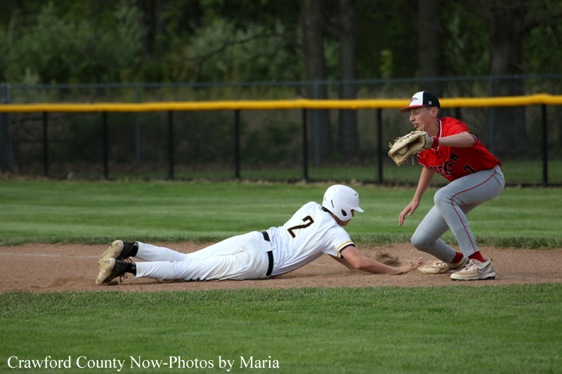 Baseball scene: a white-uniform runner slides headfirst into a dirt base while a red-uniform fielder reaches with a glove to tag him nearby on the infield fielding position.