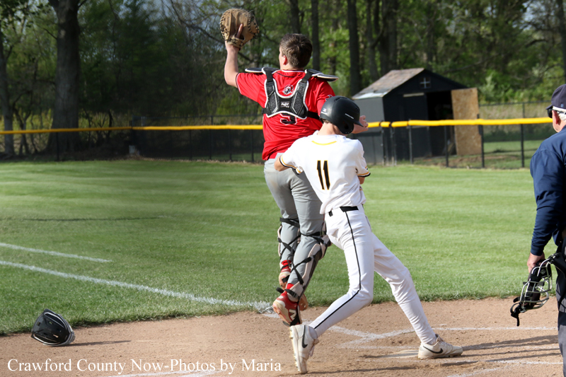 Baseball play at the base: a runner in white slides toward home as the catcher in red and protective gear reaches up to catch the ball; helmet lies on the dirt nearby.