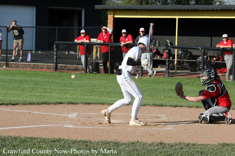 Baseball batter in white swings at a pitch as the catcher in red gear crouches at home plate; ball is in midair.