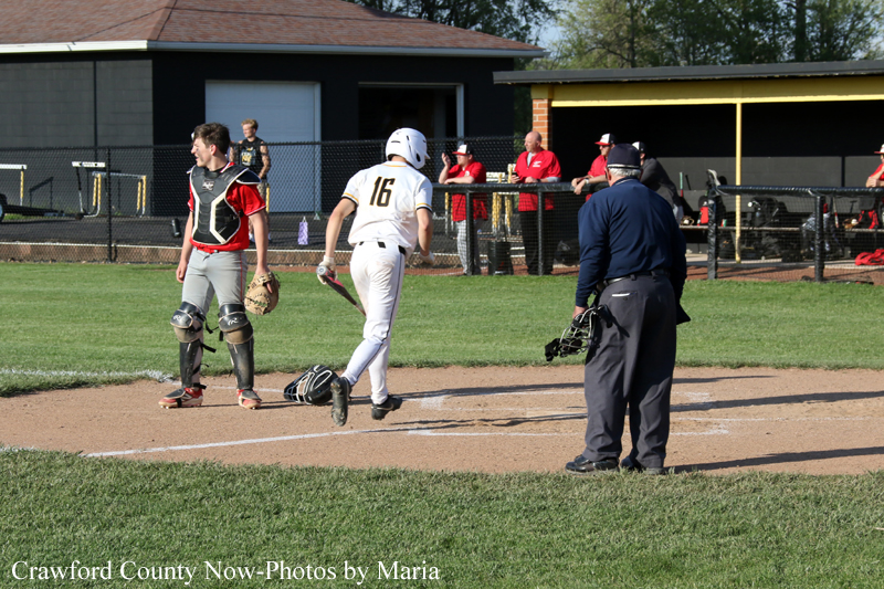Youth baseball scene: runner in white (#16) heads to first past the catcher near home plate as the umpire watches.
