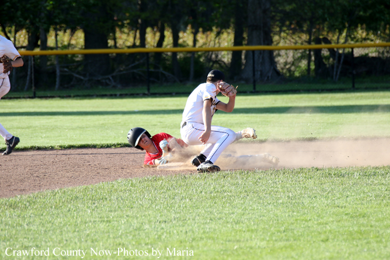 Baseball play on the infield: a white-uniform infielder tags a sliding runner in red as a dust cloud rises behind them.