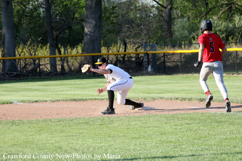 Baseball action: a fielder in white dives on the dirt to field a ground ball, glove outstretched as a runner in red watches nearby