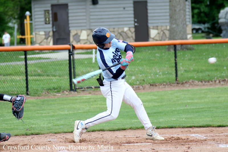 Baseball batter in white and navy uniform swings a bat during a game on a grassy field, helmeted and focused on the ball.