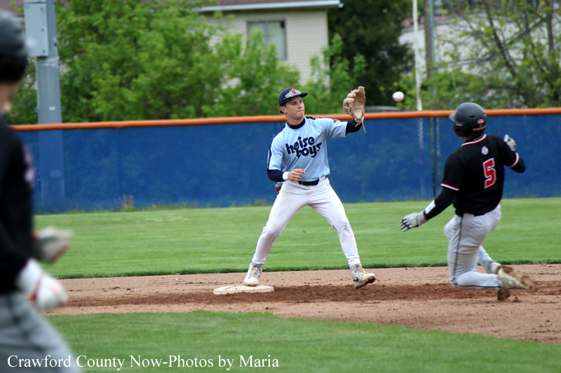 Pitcher in a light blue uniform winds up to throw from the mound as a baserunner in black slides toward second base nearby.
