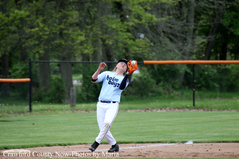 Baseball player in a light-blue uniform catches a ball on a grassy field with orange foul poles in the background.