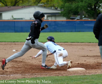 Baseball action: a baserunner in black speeds past a sliding fielder in light blue near the base on a dirt infield.