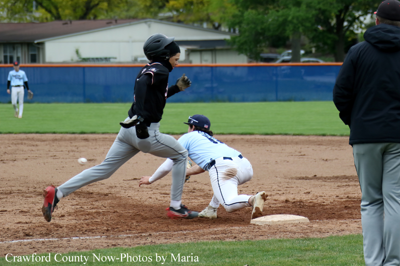 Baseball action: a baserunner in black speeds past a sliding fielder in light blue near the base on a dirt infield.