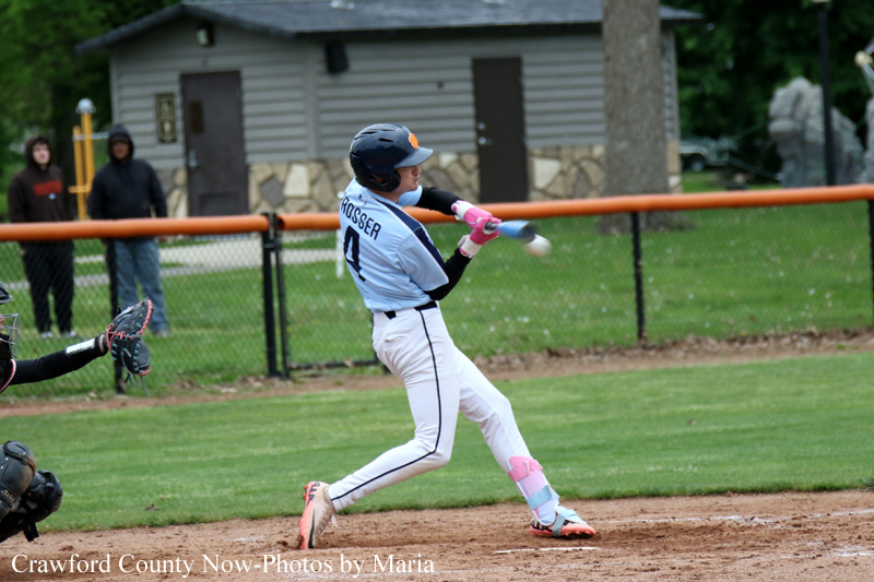 Baseball batter in a light blue uniform swings at a pitch on a grassy field.