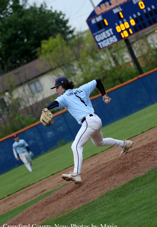 Baseball pitcher in a light-blue uniform throws from the mound with a scoreboard and outfield wall in the background.