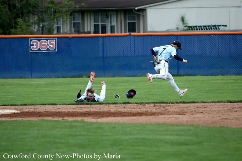 Two baseball players clash in an infield play: a runner slides on the grass as a fielder jumps over him and the ball is nearby.