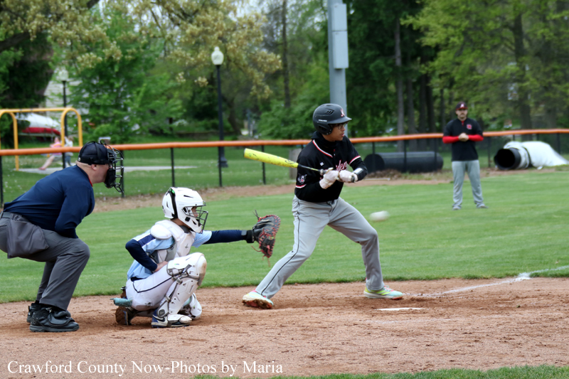 Baseball batter in black swings at a pitch as the catcher in white gear crouches at home plate.