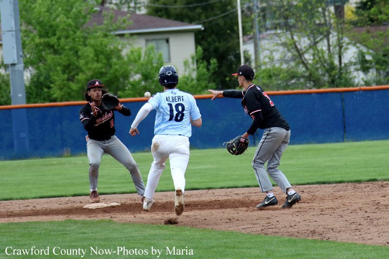 Baseball infield action as a runner in a light-blue jersey (#18, Albert) advances toward second while a Black-clad fielder and a teammate look on.