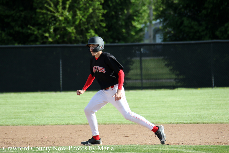 Baseball player sprinting on a dirt infield, wearing a black jersey with red sleeves, a helmet, and white pants.