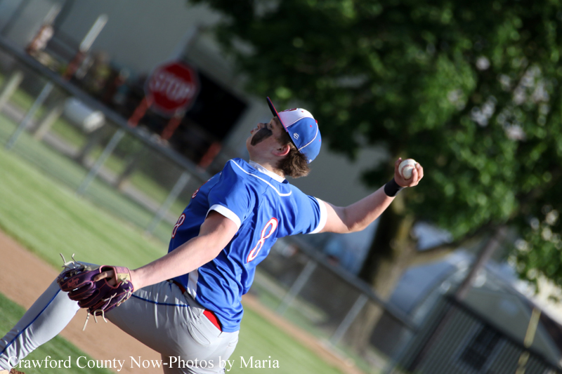 Baseball pitcher in a blue uniform winding up to throw a pitch on a sunny field.