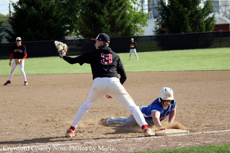 Baseball infield moment: a fielder in black reaching with his glove toward a blue-uniform runner sliding into the base, with dust rising.