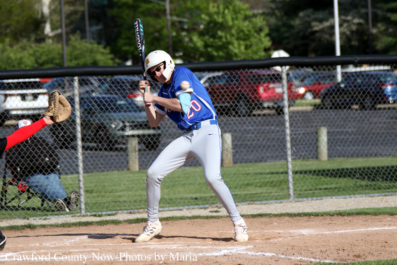 Baseball batter in a blue uniform and white helmet stands in the batter's box, ready to swing with a bat raised.
