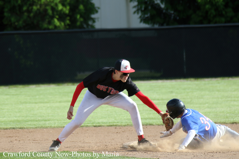 Baseball field scene: a fielder in black and red leans to tag a sliding baserunner in blue as dust rises at the base edge.