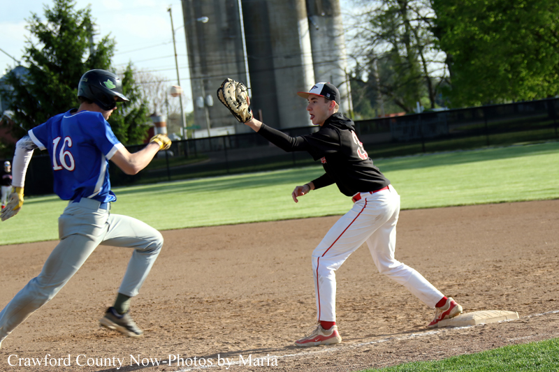 Baseball game action: runner in blue (#16) sprinting toward first as a fielder in black reaches with his glove to make the play at the bag at first base.