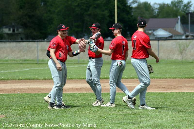 Four baseball players in red jerseys high-fiving on a baseball field after a play.