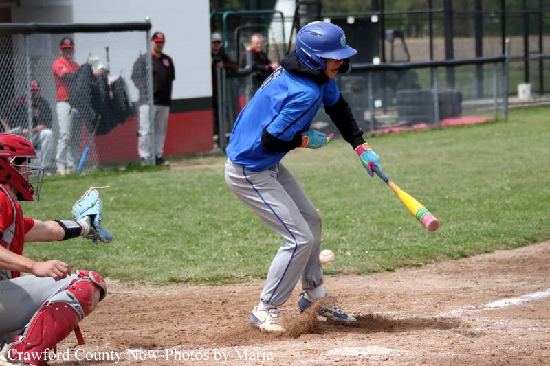 Youth baseball batter in blue swings at a pitch near home plate as the catcher in red prepares.