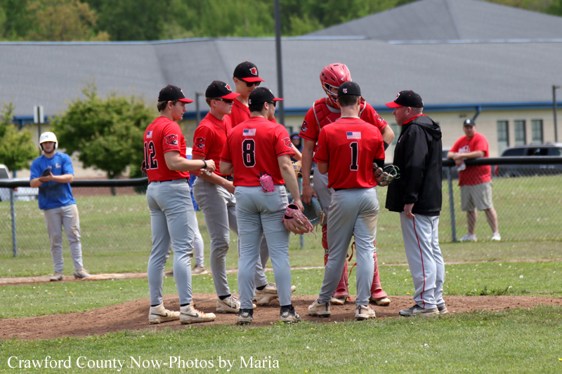 Baseball team in red uniforms huddles on the pitcher's mound during a game.