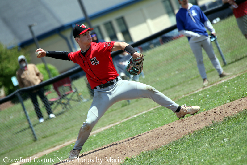 Baseball pitcher in a red uniform winds up to throw a pitch on the mound during a game.