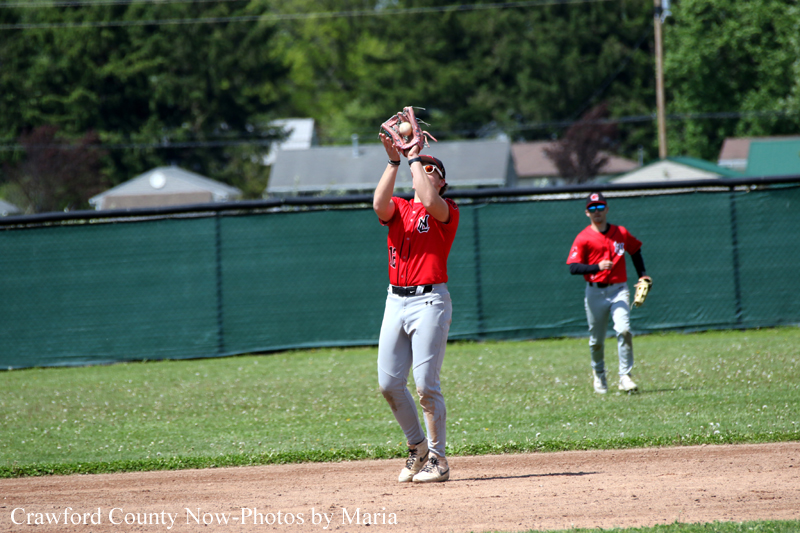Baseball player in red jersey catches a high pop foul on infield dirt, with another fielder in red in the background.