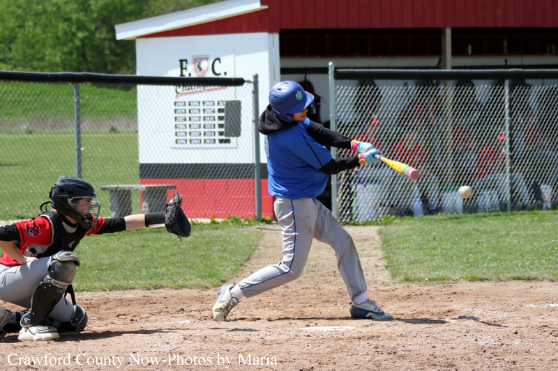 Youth baseball: a batter in blue swings at a pitch with the catcher in red/black crouched behind him on the dirt infield.